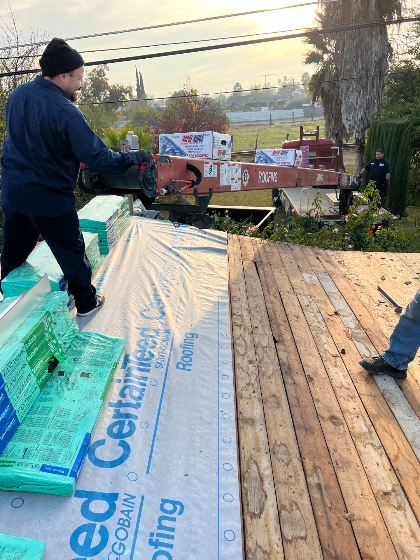 Crew loading shingle bundles onto a roof with CertainTeed underlayment and roofing conveyor
