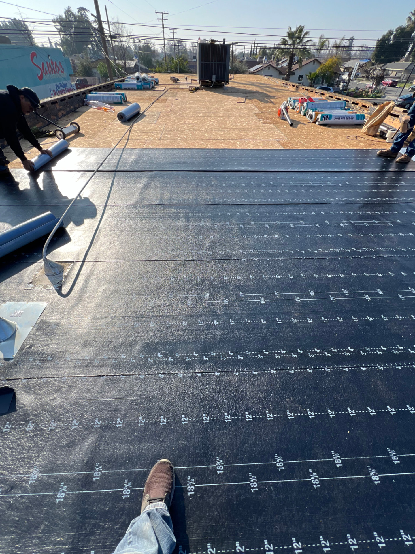 Crew rolling base sheet across a commercial flat roof deck