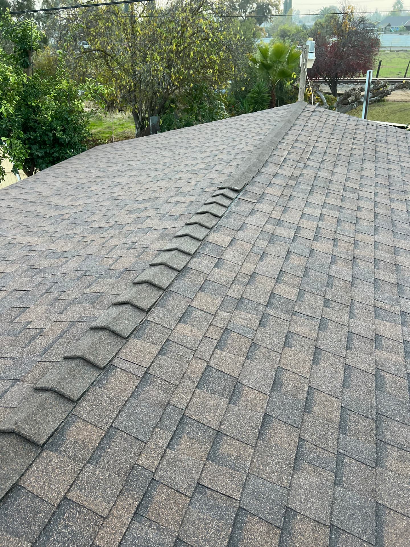 Completed architectural shingle roof with straight ridge caps in a residential neighborhood